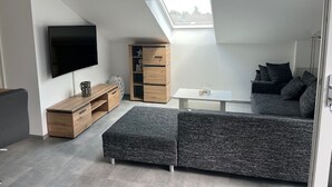 A modern loft apartment with a large skylight, a flat-screen TV, a wooden cabinet, a grey sectional sofa, and a small white table. - "Weiher Lounge" vacation apartment in the tranquil village of Huppenbroich (Simmerath)