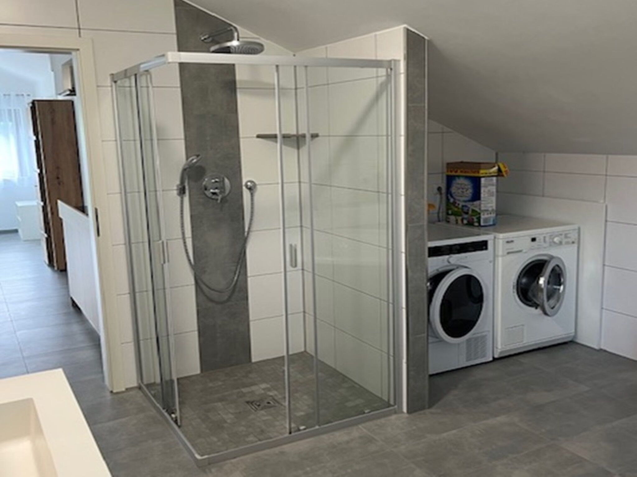 Een moderne badkamer met een glazen douchecabine, een ingebouwde wasmachine en een betegelde vloer.