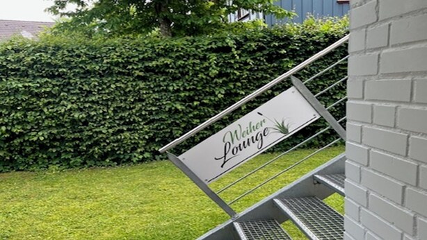 A metal staircase with a sign reading "Weiher Lounge" leading to a grassy area. - "Weiher Lounge" vacation apartment in the tranquil village of Huppenbroich (Simmerath)