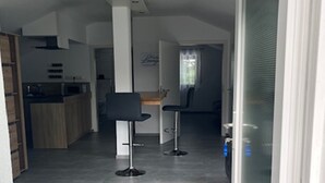 A modern kitchen with a central island, two bar stools, and a dining area with a window. - "Weiher Lounge" vacation apartment in the tranquil village of Huppenbroich (Simmerath)