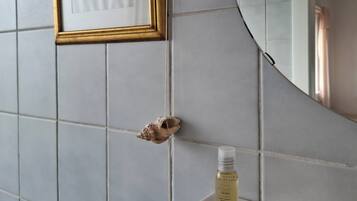 A bathroom with a tiled wall, a framed picture, a mirror, and a bottle of shampoo on a shelf.