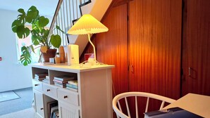 Una habitación con un escritorio blanco, una silla, una estantería, una planta en maceta, una lámpara y un armario de madera.