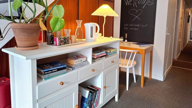 Un escritorio con una planta en maceta, una lámpara y una pizarra con la palabra 'Welcome' escrita.