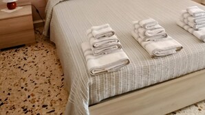 Un lit bien fait, avec des serviettes pliées, une tête de lit et un tableau de fleurs accroché au mur.