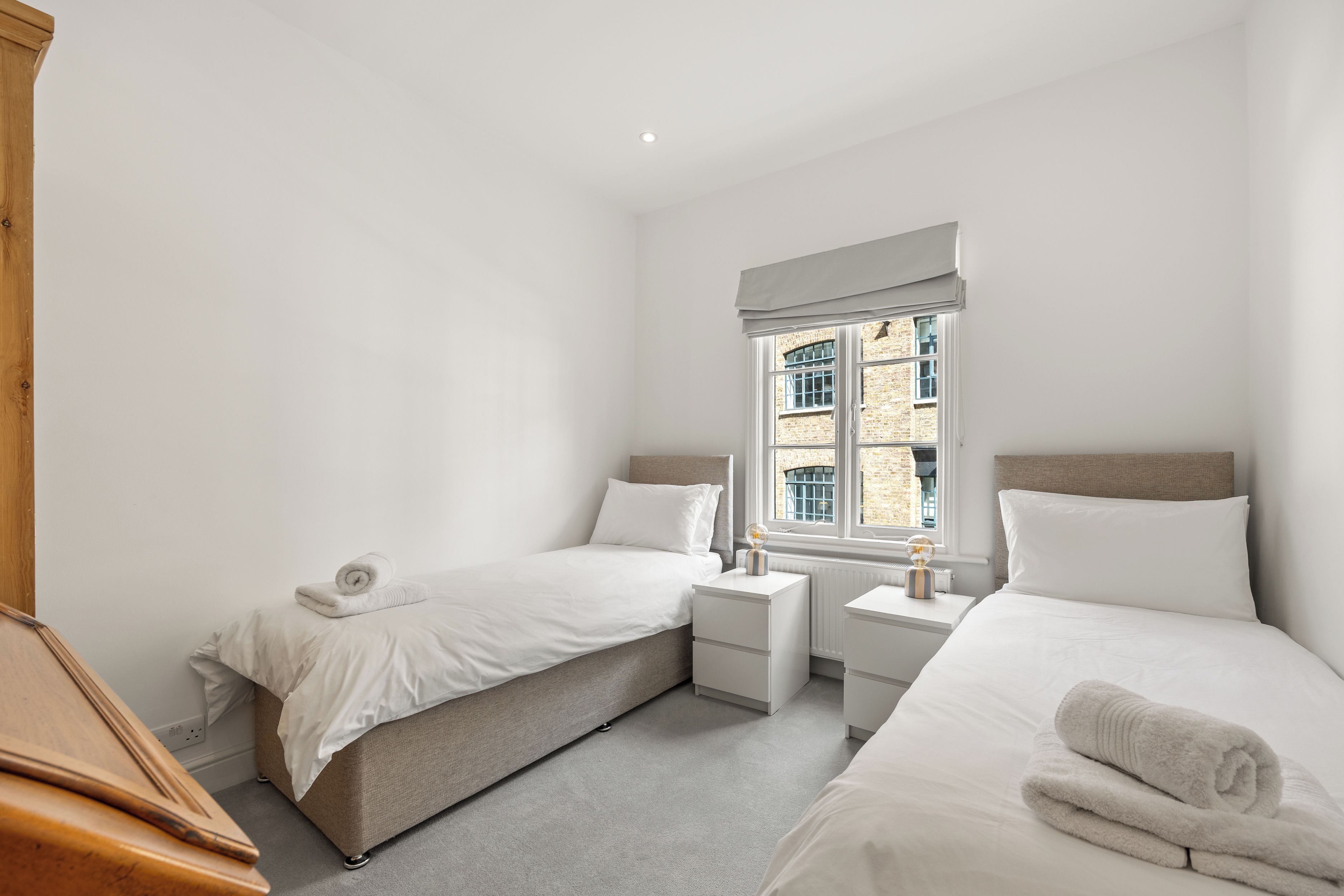 A bedroom with two beds, a window with a view of a brick building, and a radiator on the wall.