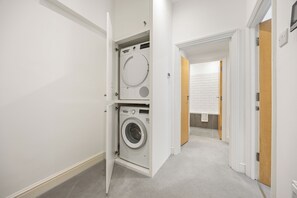 Un lavadero con lavadora y secadora de carga frontal, pared de azulejos blancos y puerta de madera que da a un baño.