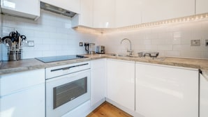 Eine moderne Küche mit weißen Schränken, einem Einbauofen, einem Spülbecken und einer Arbeitsplatte mit Kaffeemaschine und Toaster.