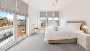 Ein modernes Schlafzimmer mit großem Fenster, einem Bett, einem Nachttisch und einem Sessel.