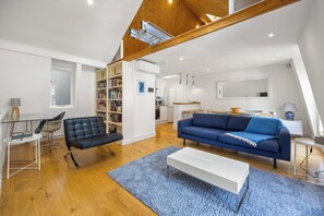 Ett modernt vardagsrum med en svart lädersoffa, en blå soffa, ett vitt soffbord och en bokhylla.