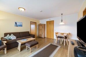 Una sala de estar con sofá, mesa de centro, mesa de comedor, sillas, televisor y chimenea.