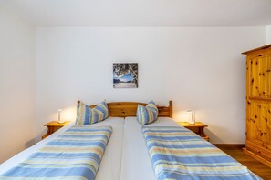 Una cama doble con ropa de cama a rayas, dos mesitas de noche con lámparas, un cabecero de madera y un armario de madera, además de un cuadro en la pared.