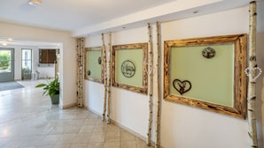 A hallway with framed artwork on the walls, a potted plant, and a door leading to another room.