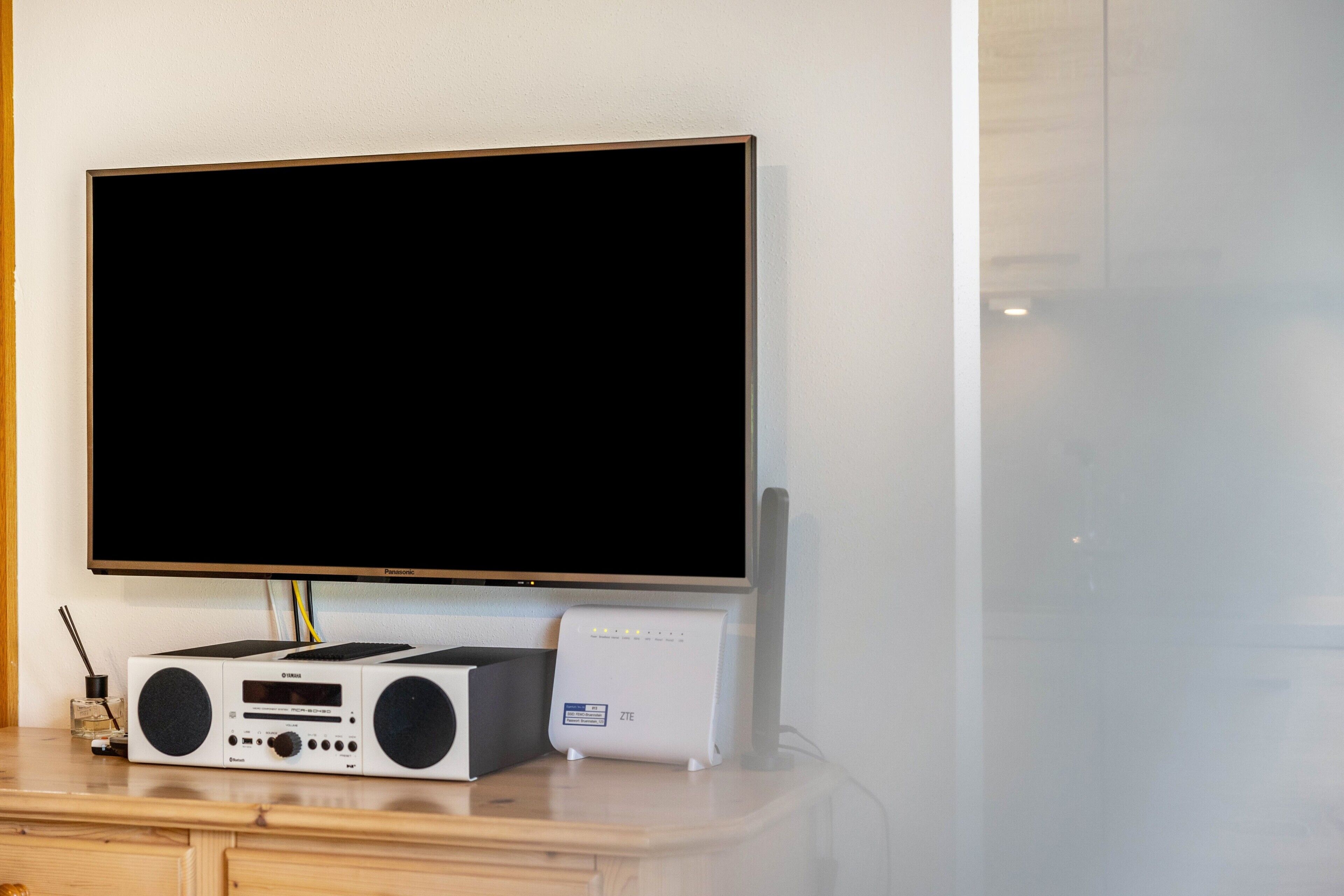 Un televisor de pantalla plana montado en la pared, un equipo de sonido y un dispositivo blanco sobre una superficie de madera.