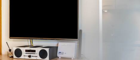 Un televisor de pantalla plana montado en la pared, un equipo de sonido y un dispositivo blanco sobre una superficie de madera.