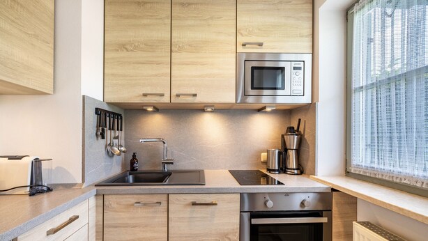 Eine moderne Küche mit Holzschränken, einer Edelstahl-Mikrowelle, einem Spülbecken und einem Backofen.