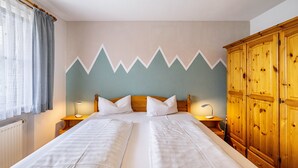Una cama doble con sábanas blancas, dos mesitas de noche con lámparas, un armario de madera y una pared con diseño en zigzag.
