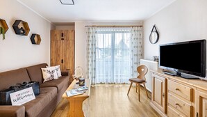 Una sala de estar con sofá, mesa de centro, televisor, aparador de madera y ventana con cortinas.