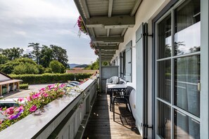 A covered outdoor area with a wooden deck, a table with chairs, and a row of windows.
