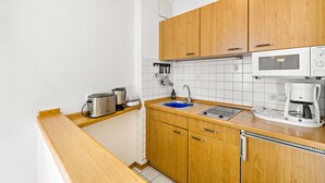 Una cocina compacta con armarios de madera, microondas integrado, cafetera y lavamanos.