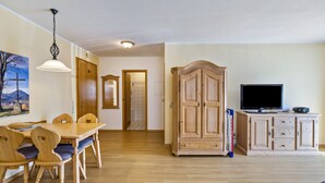 Un área de comedor con una mesa y sillas de madera, un televisor sobre un mueble bajo y un pasillo que conduce a otra habitación.