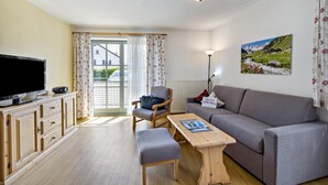 Una sala de estar con televisión, sofá, mesa de madera y una silla.