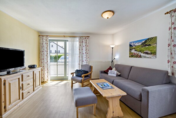 A living room with a television, sofa, wooden table, and a chair.