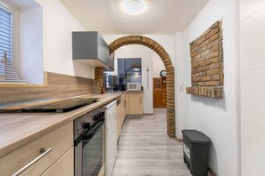 A narrow kitchen with a brick archway, wooden cabinets, a microwave, and a trash bin.