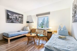 A bedroom with a bed, a desk, two chairs, a window, and a wall-mounted lamp.