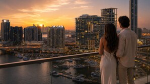 Un couple se tient sur un balcon, surplombant une marina avec des bateaux et des immeubles de grande hauteur en arrière-plan.