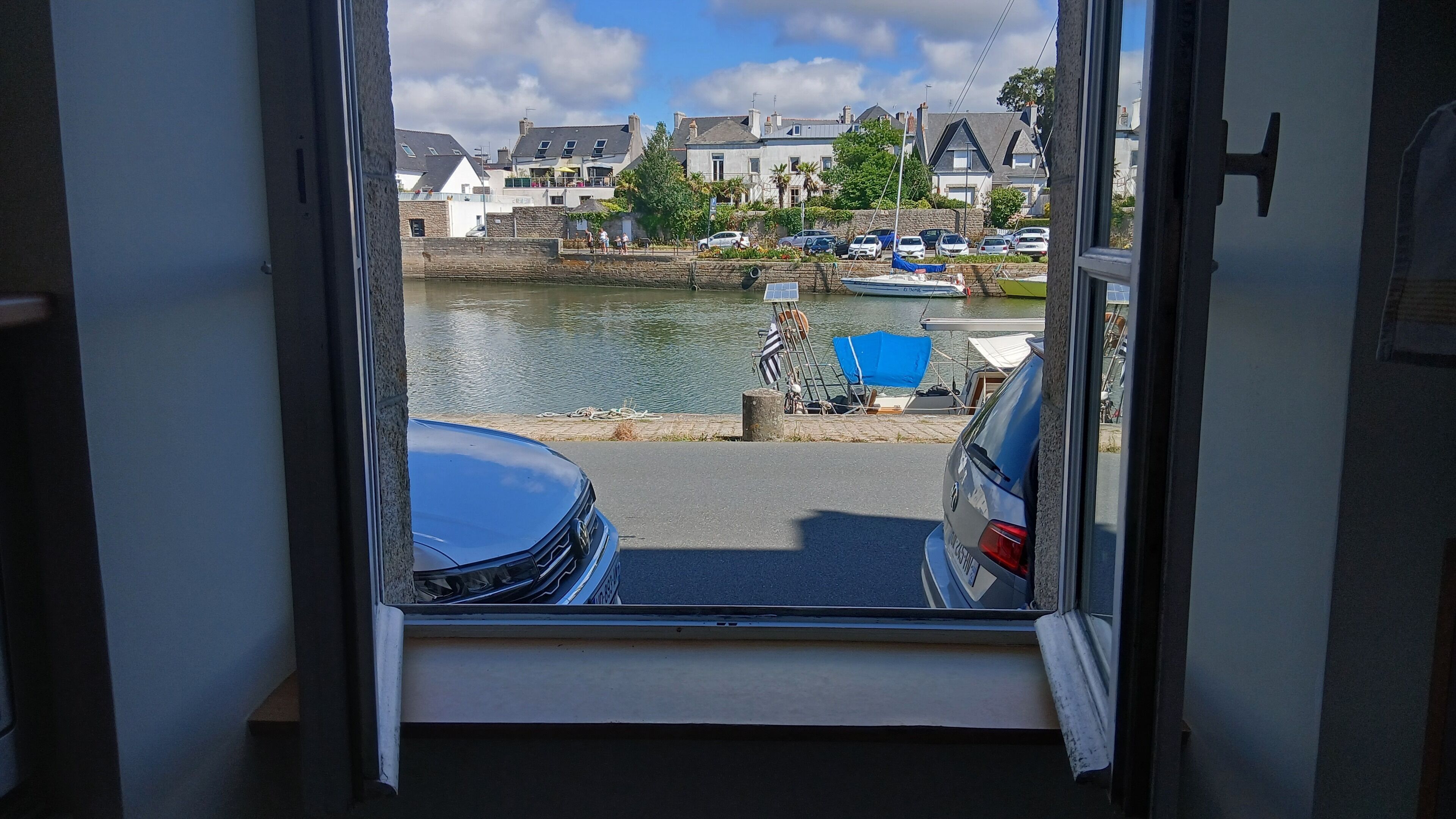 Blick aus einem Zimmer auf einen Hafen mit Booten, einem Auto und Gebäuden im Hintergrund.