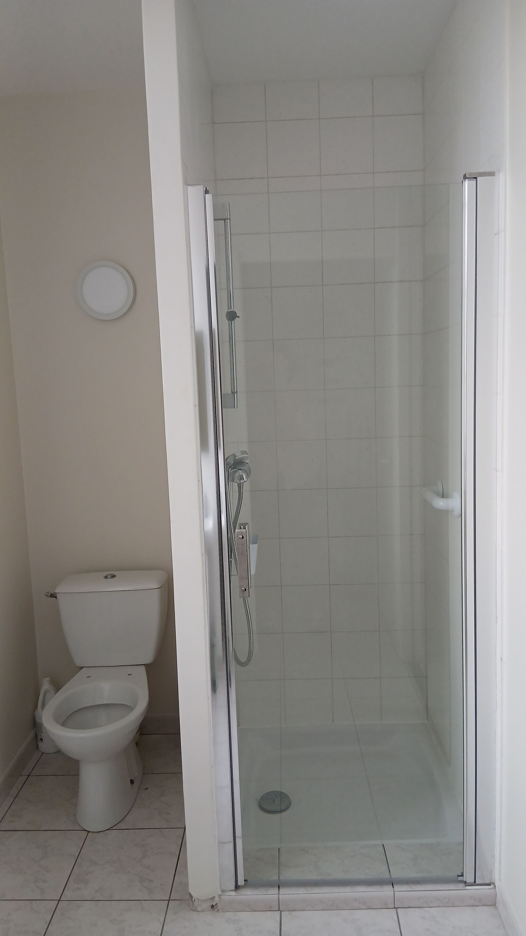 Un baño con inodoro, ducha con puerta de vidrio y paredes de azulejos.