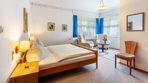 A hotel room with a bed, bedside table, lamp, chair, and a small table with a vase. - Double Room No. 2 with Shared Terrace, Shared Garden and Wi-Fi (Dachsberg (Südschwarzwald))