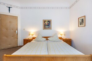 A double bed with a headboard, two bedside tables with lamps, a framed painting on the wall, and a door with a decorative panel.