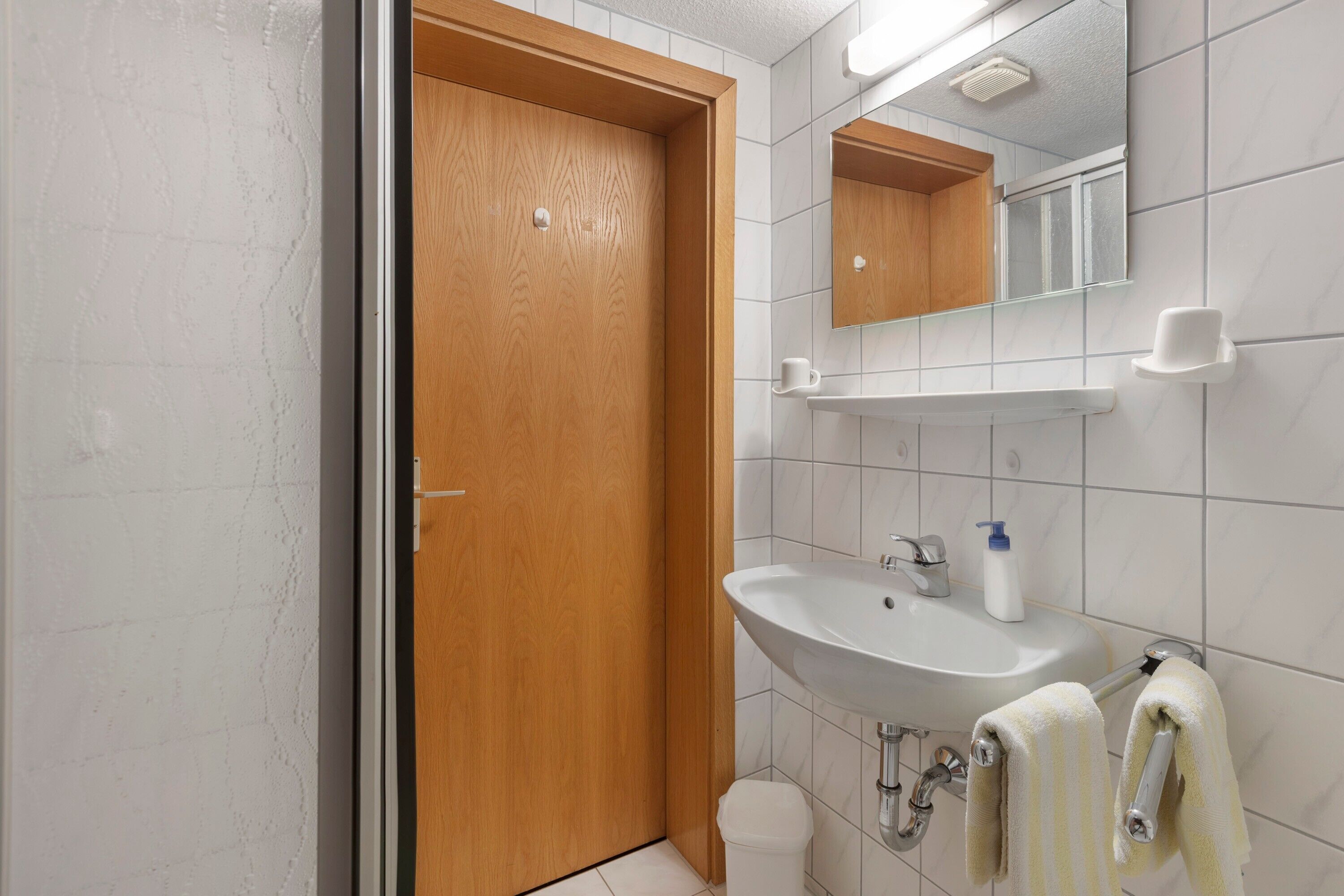 Une salle de bain avec une porte en bois, un lavabo blanc, un miroir et un porte-serviettes.