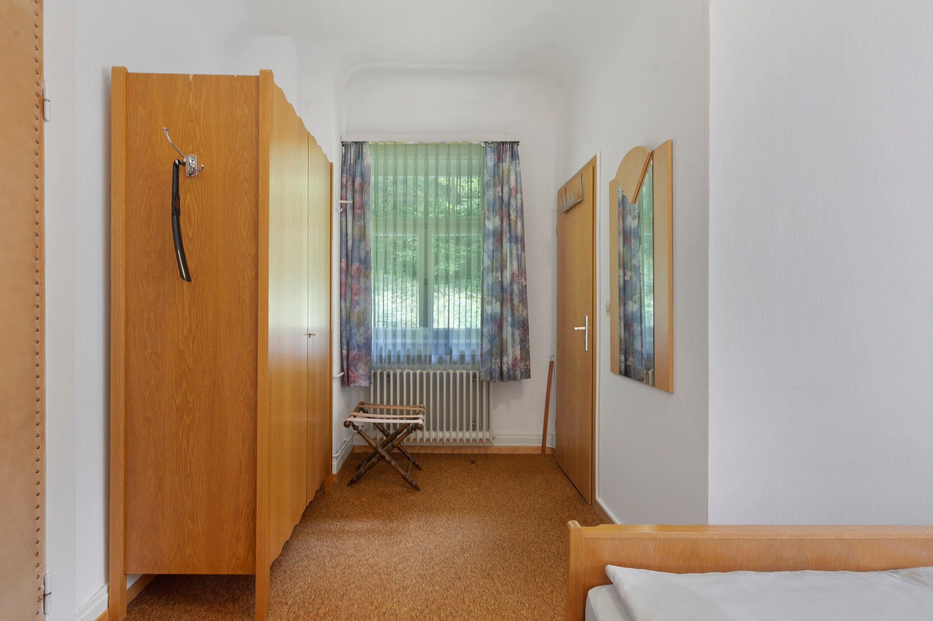 Un couloir étroit avec une porte en bois, un radiateur, une petite table pliante et un lit au fond.