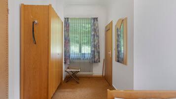 Un couloir étroit avec une porte en bois, un radiateur, une petite table pliante et un lit au fond.