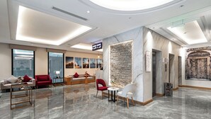 A modern lobby with a marble floor, red and white seating, a stone accent wall, and a cityscape view through large windows. - Lafait Hotel Serviced Apartments (Al Khobar)