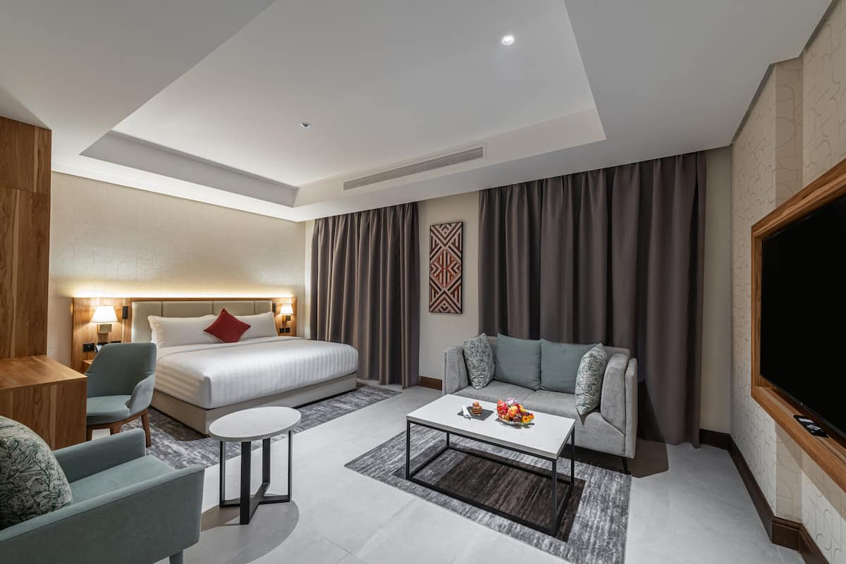 Una habitación de hotel moderna con cama, sofá, mesa de centro y televisión.