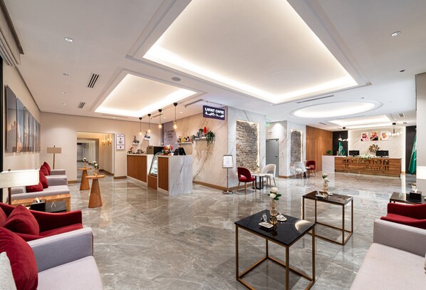 Un hall d’hôtel moderne comprenant un comptoir d’accueil, un espace salon et un bar à café.