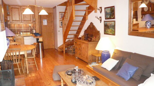 Un salon chaleureux avec un escalier en bois, un coin repas et une cuisine dotée de meubles en bois.