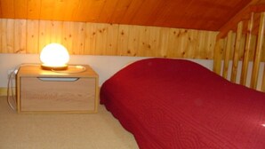 Un lit superposé en bois, avec une couverture rouge et une table de chevet dotée d’une lampe.