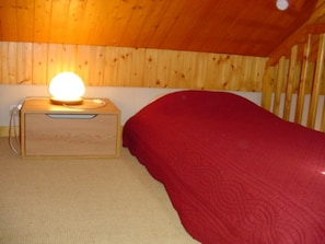Un letto a castello in legno con copripiumino rosso e un comodino con una lampada.