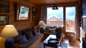 L'intérieur d'un chalet en bois chaleureux et accueillant, avec un canapé, une table et une vue sur une montagne par de grandes fenêtres.