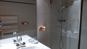 Une salle de bain avec un lavabo blanc, deux robinets et une cabine de douche en verre.
