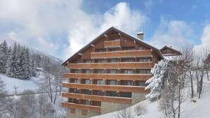 Un bâtiment en bois à plusieurs étages, doté de balcons, entouré d’arbres et de montagnes couverts de neige.