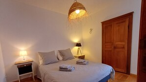A bedroom with a bed, two bedside tables, a hanging light fixture, a wooden wardrobe, and a wall-mounted light. - Charming duplex in the heart of the village of Piana (Piana)