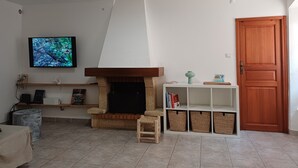 A living room with a fireplace, a television, a wooden door, and a white shelf with baskets. - Charming duplex in the heart of the village of Piana (Piana)