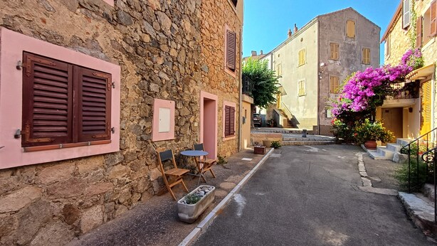 A narrow street with stone buildings, wooden shutters, and a small table with chairs. - Charming duplex in the heart of the village of Piana (Piana)