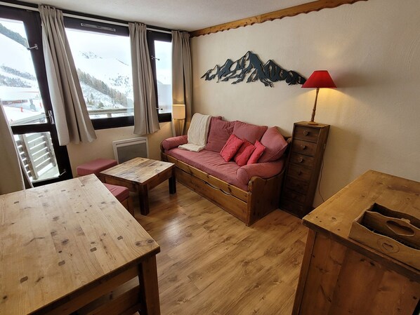 Une pièce chaleureuse avec une table en bois, un canapé à carreaux rouges et blancs, un meuble en bois et une œuvre d’art représentant une montagne accrochée au mur.