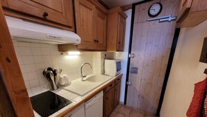 Ett kompakt kök med träskåp, en vit diskho, en mikrovågsugn och en klocka på väggen.